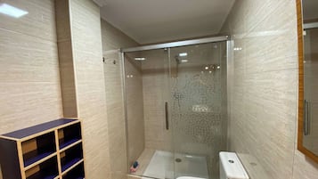 Un baño moderno con ducha de vidrio, inodoro y estantería empotrada.