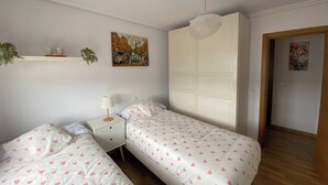 Une chambre avec deux lits simples, une table de chevet, une armoire blanche et un luminaire au plafond.
