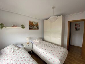 Une chambre avec deux lits simples, une table de chevet, une armoire blanche et un luminaire au plafond.
