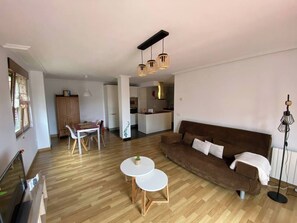 Una sala de estar moderna con un sofá marrón, dos mesas redondas blancas y un comedor con una mesa y sillas de madera.