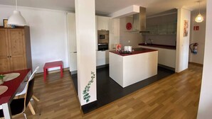 Une cuisine moderne dotée d’un îlot central, de planchers en bois et d’un coin repas avec un banc rouge.