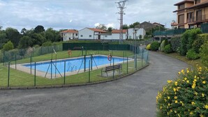Une piscine entourée d’une clôture verte, avec un banc et des bouées de sauvetage.