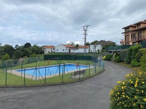 Une piscine entourée d’une clôture verte, avec un banc et des bouées de sauvetage.