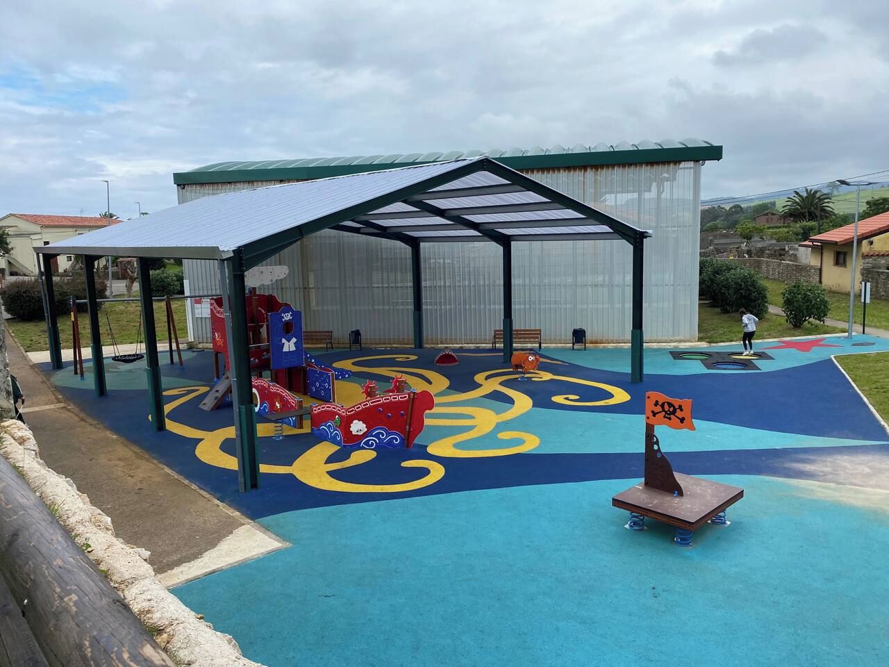 Un parque infantil con una zona de juegos cubierta, un tobogán y una bandera pirata.