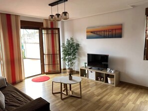 Ein Wohnzimmer mit einer Couch, einem Fernseher auf einem Schrank, einer Pflanze und einem Bild an der Wand.