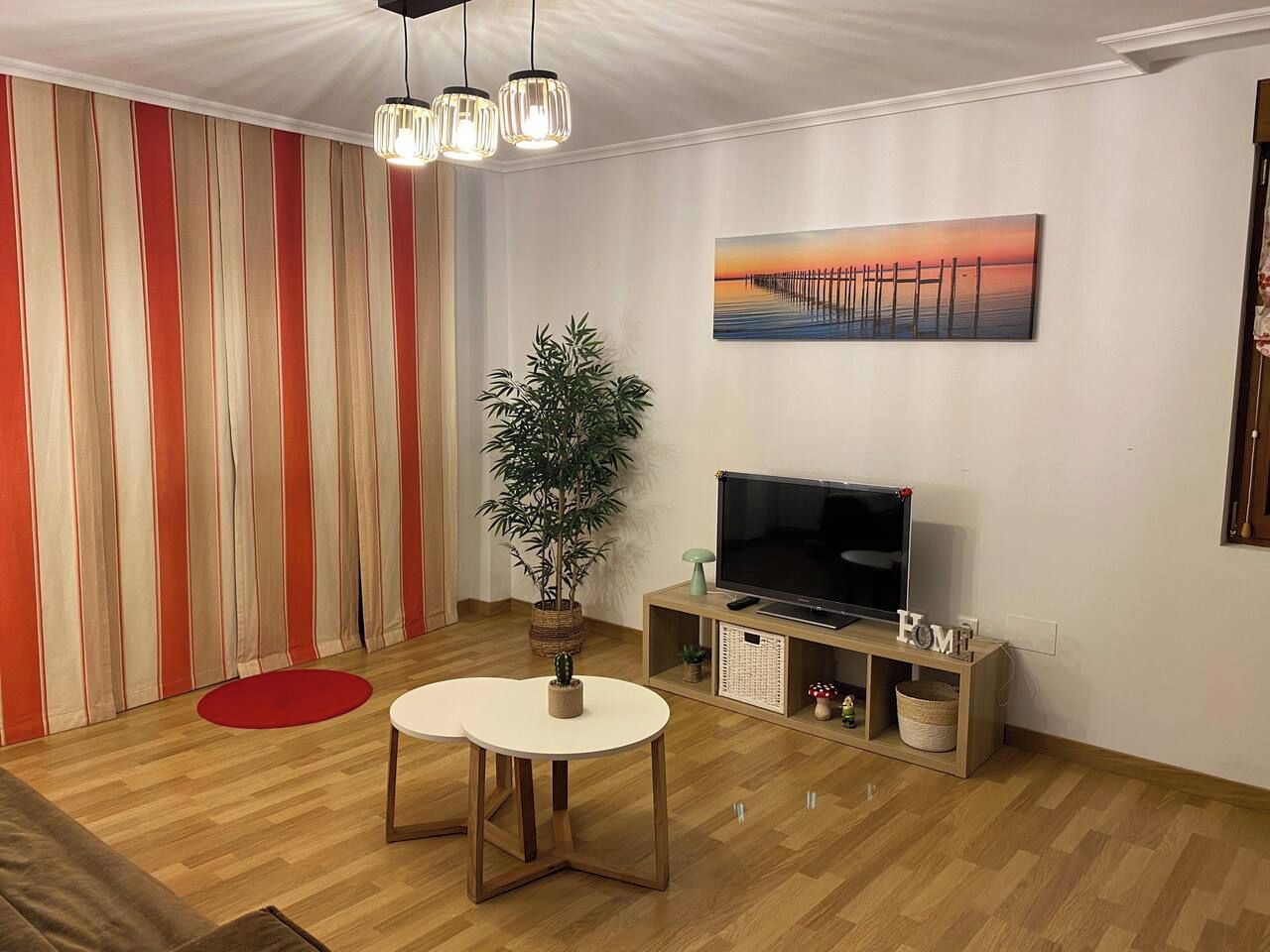 Una sala de estar con televisor, una planta y un cuadro en la pared.