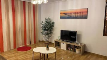 Una sala de estar con televisor, una planta y un cuadro en la pared.