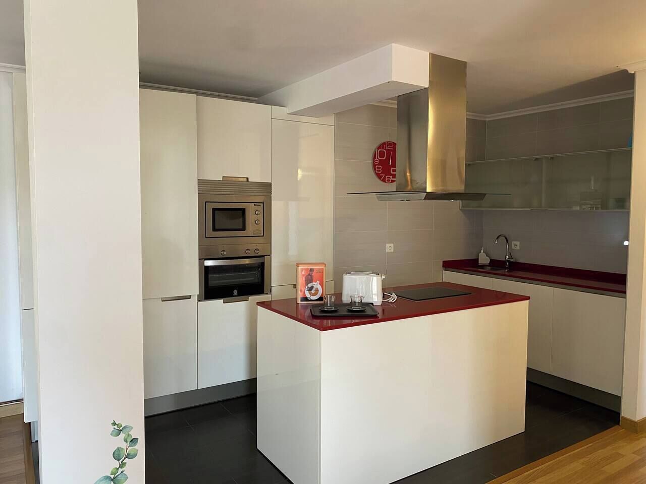 A modern kitchen with white cabinetry, a central island, a stainless steel range hood, and a red countertop.