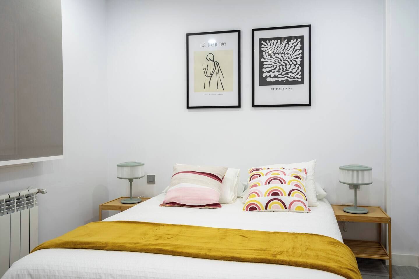Une chambre à coucher comprenant un lit, deux tables de chevet, un radiateur et deux œuvres d’art encadrées accrochées au mur.