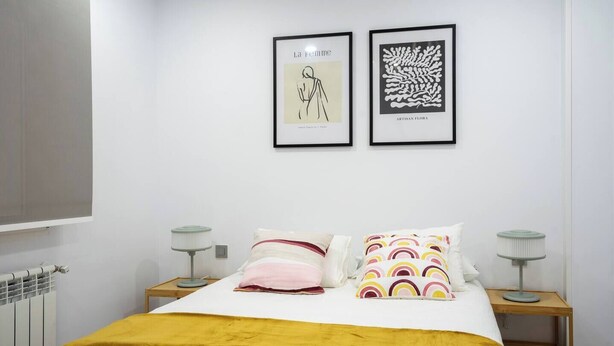 Une chambre à coucher comprenant un lit, deux tables de chevet, un radiateur et deux œuvres d’art encadrées accrochées au mur.