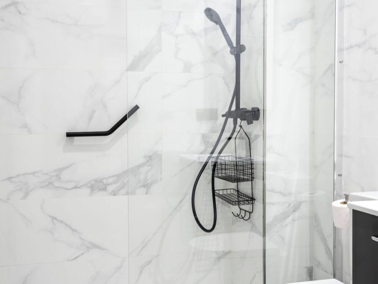 Een badkamer met een douche met glazen wand, een zwarte handdoekhouder en een toiletpapierhouder.