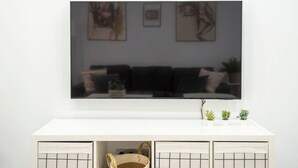 Un salon doté d’un grand téléviseur à écran plat fixé au mur, d’une console blanche avec des rangements et d’une plante en pot posée sur la console.