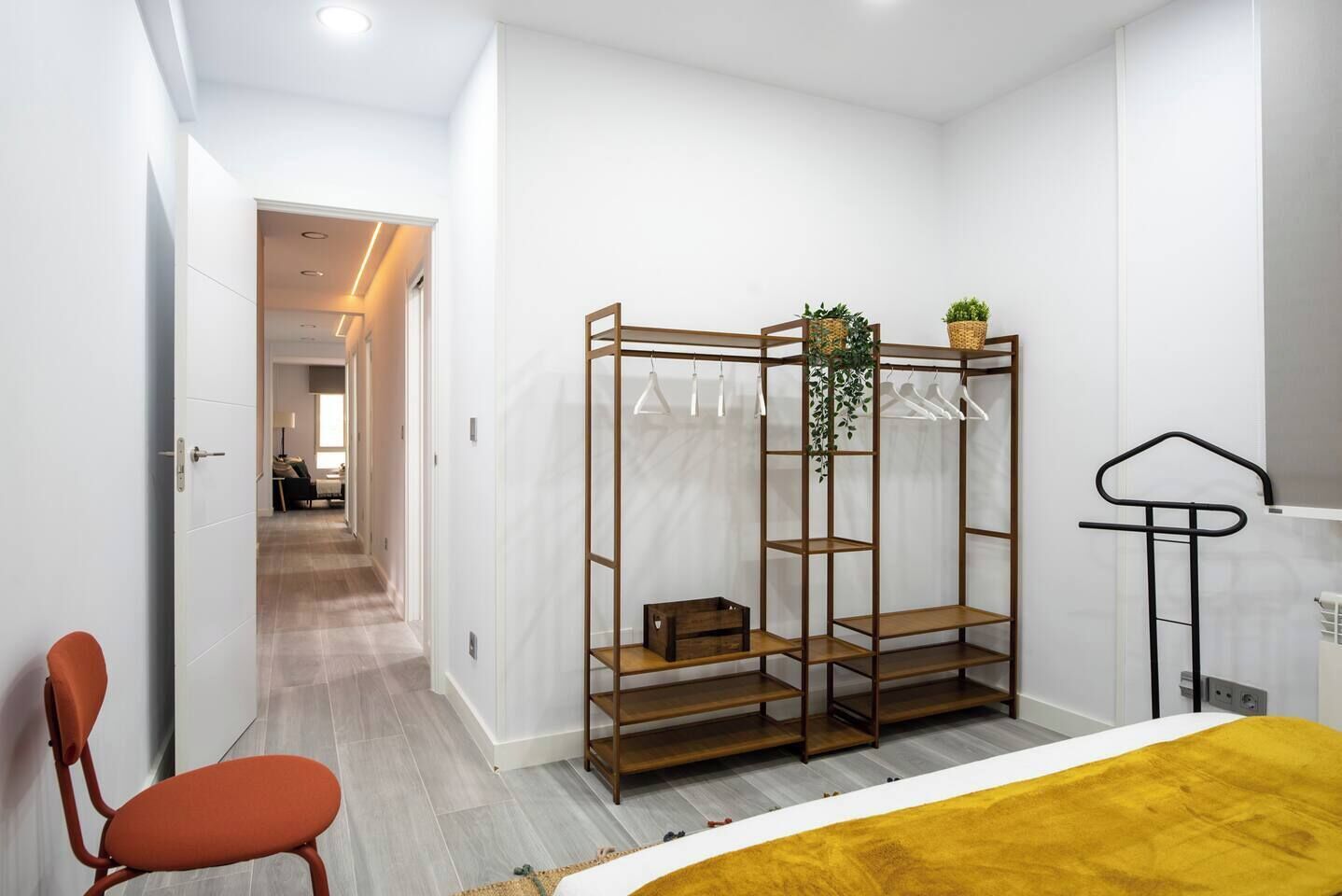 A modern bedroom with a bed, a wooden wardrobe, a chair, and a hanging plant.