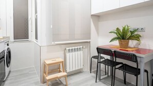 Une petite cuisine équipée d’un lave-linge, d’un radiateur, d’un petit tabouret en bois et d’une table avec deux chaises.
