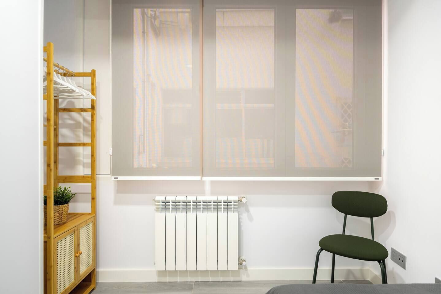 Een kamer met een radiator, een houten plank met hangende spullen, en een stoel.