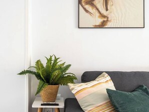 Una habitación con un sofá gris, un cojín a rayas, un cojín verde y una planta de helecho en una mesita.