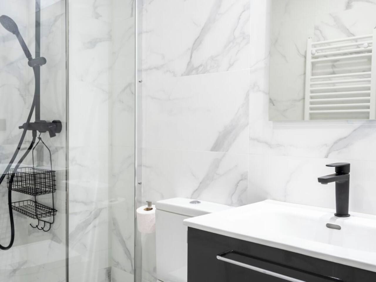 Een moderne badkamer met een glazen douchecabine, een witte marmeren wand, een zwarte kraan en een wit aanrecht.