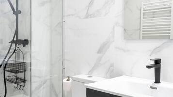 Een moderne badkamer met een glazen douchecabine, een witte marmeren wand, een zwarte kraan en een wit aanrecht.
