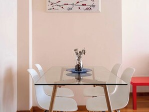 A modern dining area with a glass table, white chairs, and a red table on the right. - Apartamento en Entrambasaguas Centro (Entrambasaguas)
