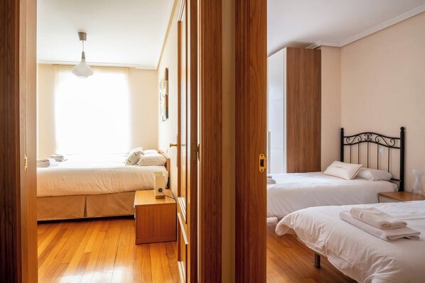 A hotel room with two beds, wooden flooring, a bedside table, and a window with natural light. - Apartamento en Entrambasaguas Centro (Entrambasaguas)