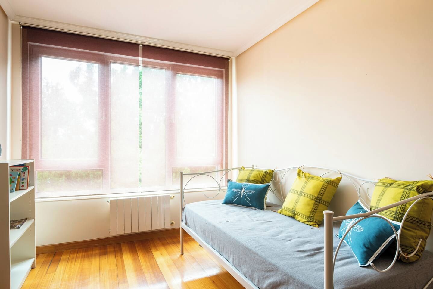 A room with a bed, a radiator, a window, and a bookshelf.