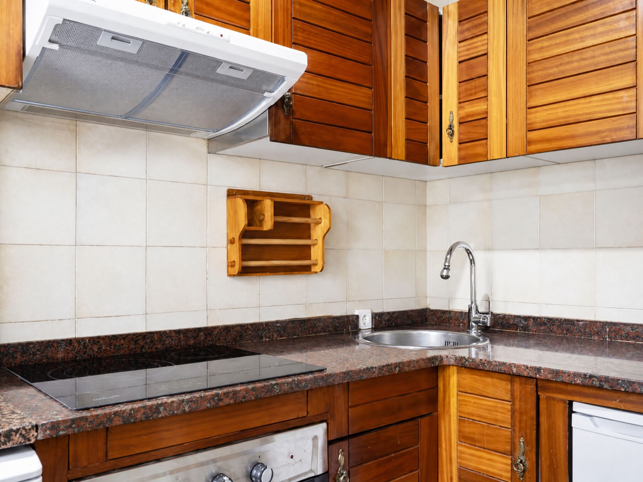 Una cocina con gabinetes de madera, encimera de granito, pileta de acero inoxidable y horno empotrado.
