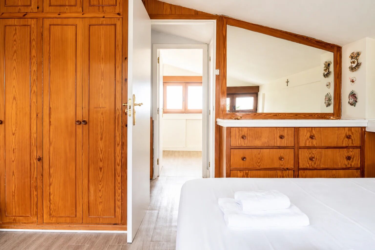 Ein Schlafzimmer mit einem Holzschrank, einem großen Spiegel und einem ordentlich bezogenen Bett.