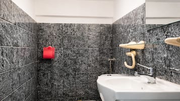 A bathroom with a white sink, a mirror, and a shower area with a towel rack.