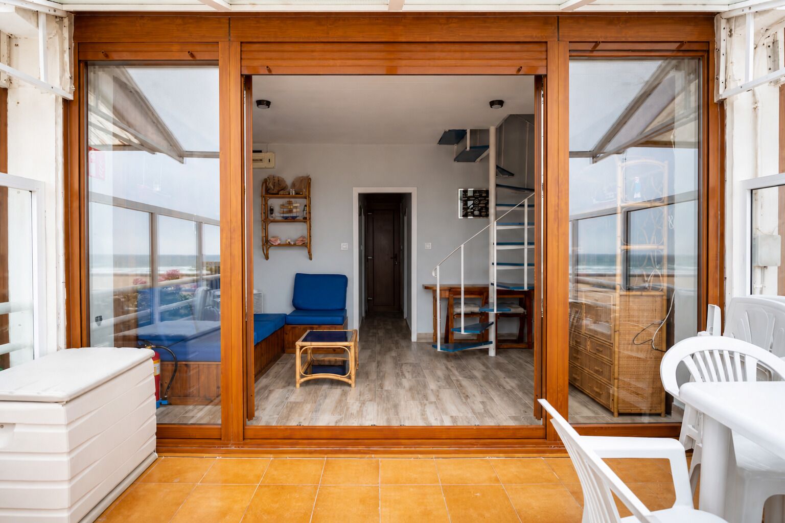 Ein Zimmer mit Holzboden, einem blauen Sofa, einem weißen Sessel, einem kleinen Tisch und einer Treppe, die in eine obere Ebene führt.