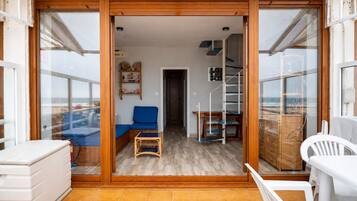 Ein Zimmer mit Holzboden, einem blauen Sofa, einem weißen Sessel, einem kleinen Tisch und einer Treppe, die in eine obere Ebene führt.