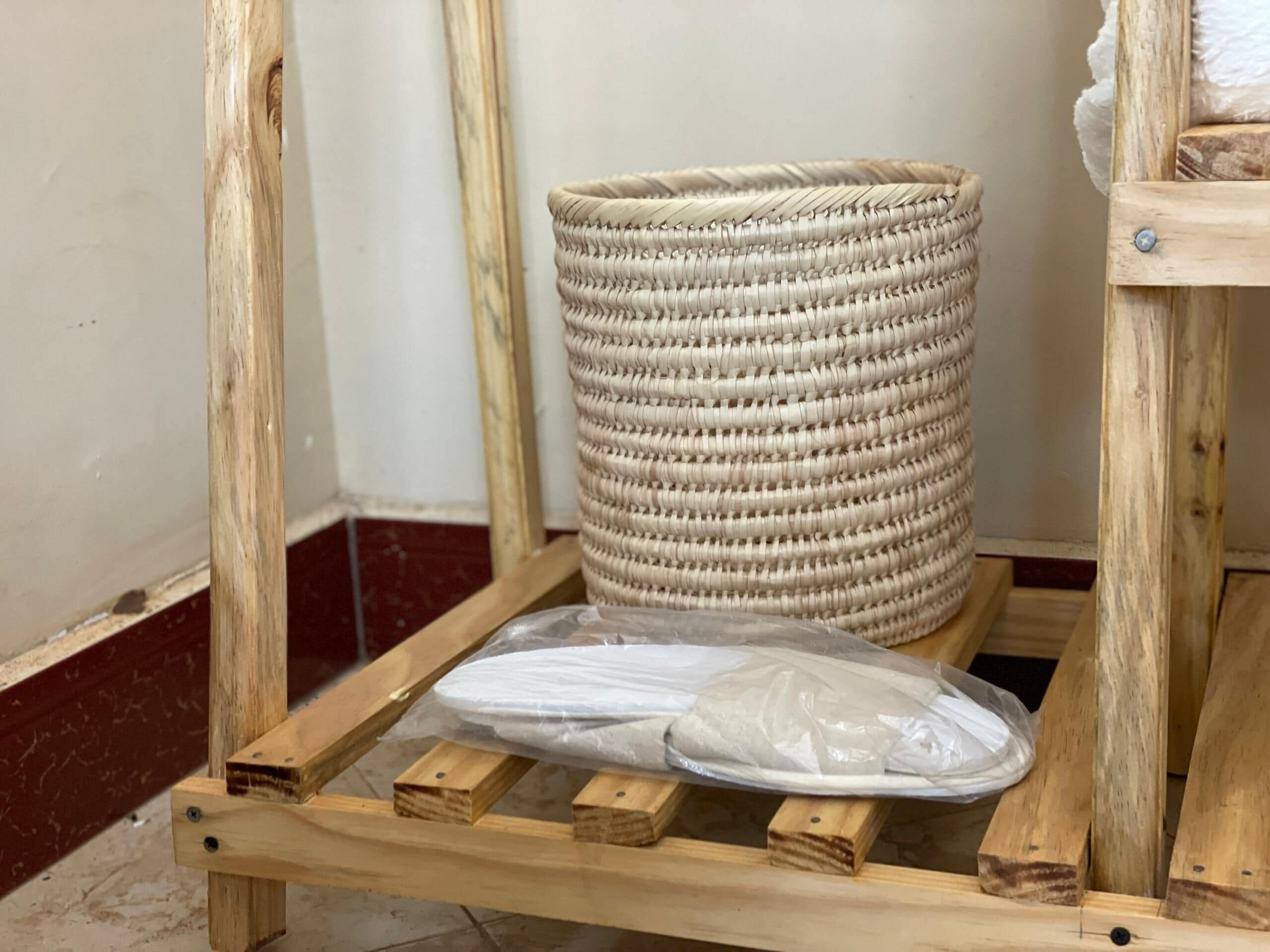 Una cesta tejida sobre un soporte de madera, con un objeto envuelto en plástico debajo.