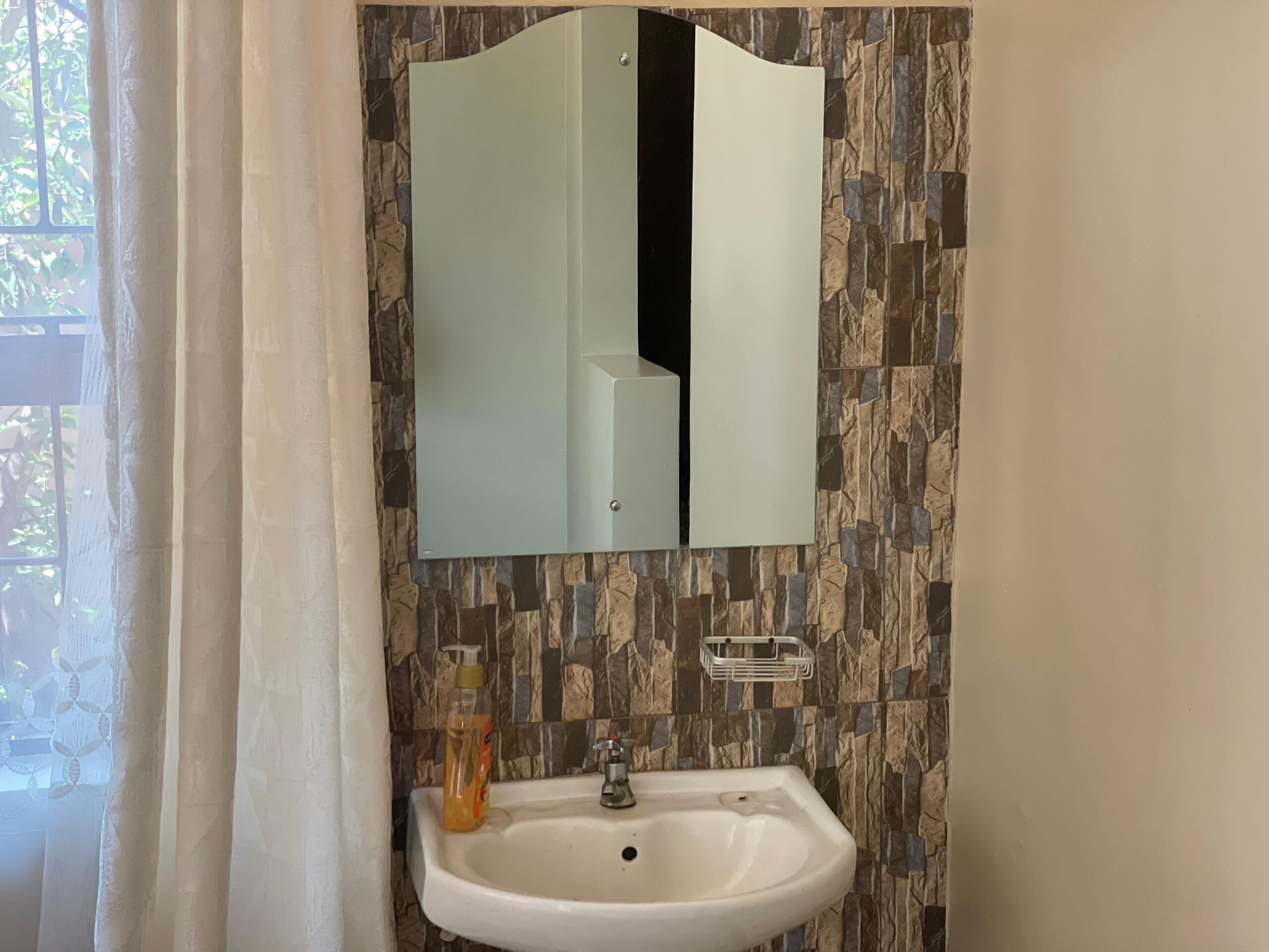 A bathroom with a white sink, a mirror, and a stone-patterned wall.