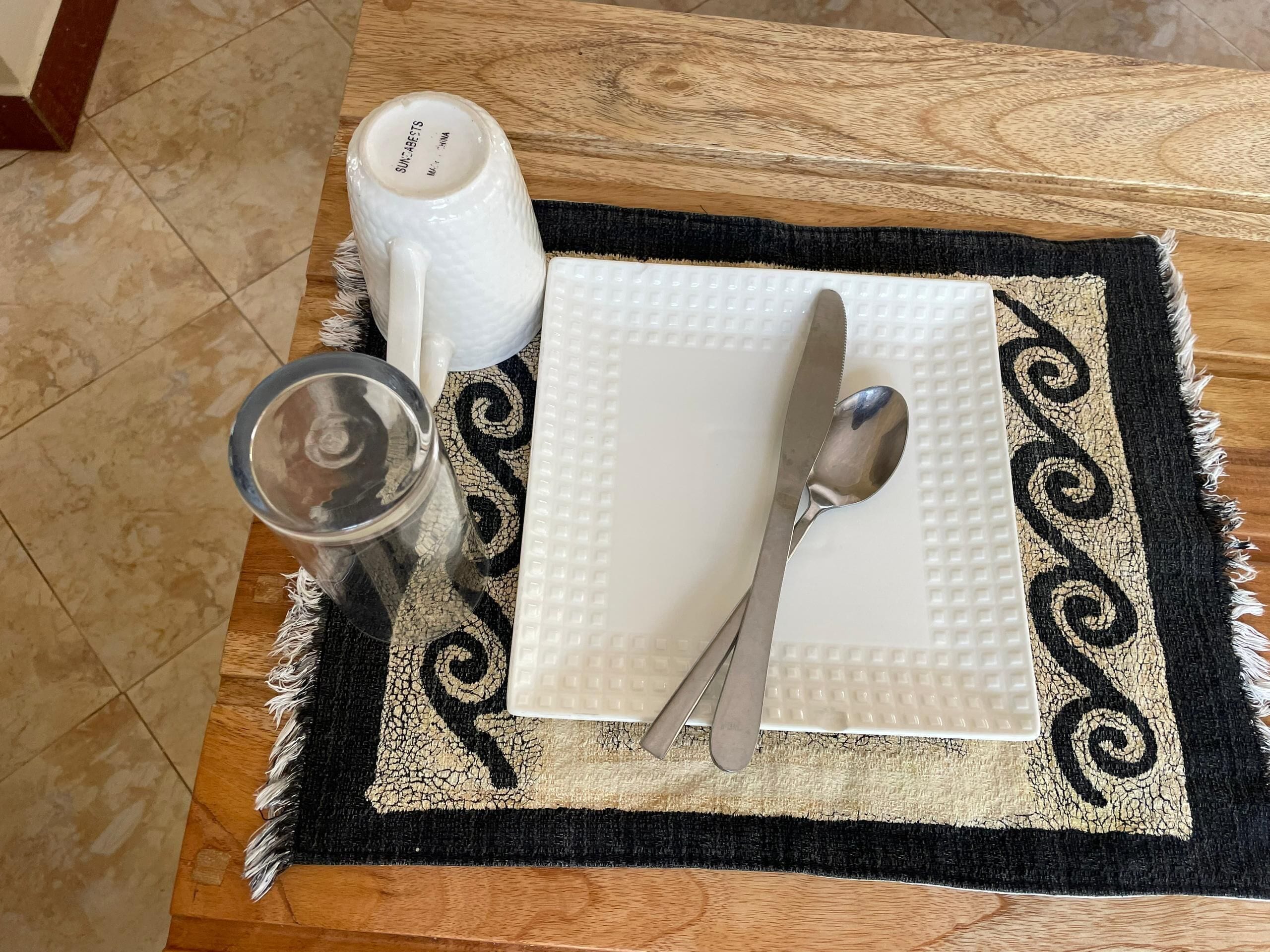 A table set with a white placemat, a white napkin, a spoon, a glass, and a salt and pepper shaker.