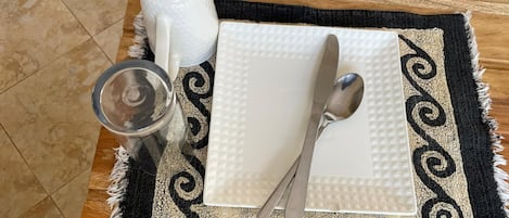 A table set with a white placemat, a white napkin, a spoon, a glass, and a salt and pepper shaker.