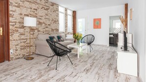 Een woonkamer met een bakstenen muur, een bank, twee stoelen, een salontafel en een tv-meubel.