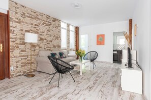 A living room with a brick wall, a sofa, two chairs, a coffee table, and a TV stand. - Apartamento de 4 habitaciones en Santander (Santander)