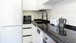 Een moderne keuken met witte kastjes, een zwart aanrecht, een magnetron, een broodrooster en een koffiezetapparaat.