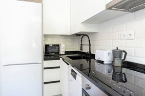 A modern kitchen with white cabinetry, a black countertop, a microwave, a toaster, and a coffee maker. - Apartamento de 4 habitaciones en Santander (Santander)