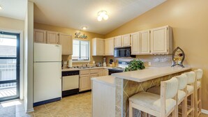 A kitchen with light wooden cabinets, a refrigerator, a microwave, a sink, and a bar area with stools. - Waterfront Lazy Days Condo w/ Views & Pool Access! (Osage Beach)