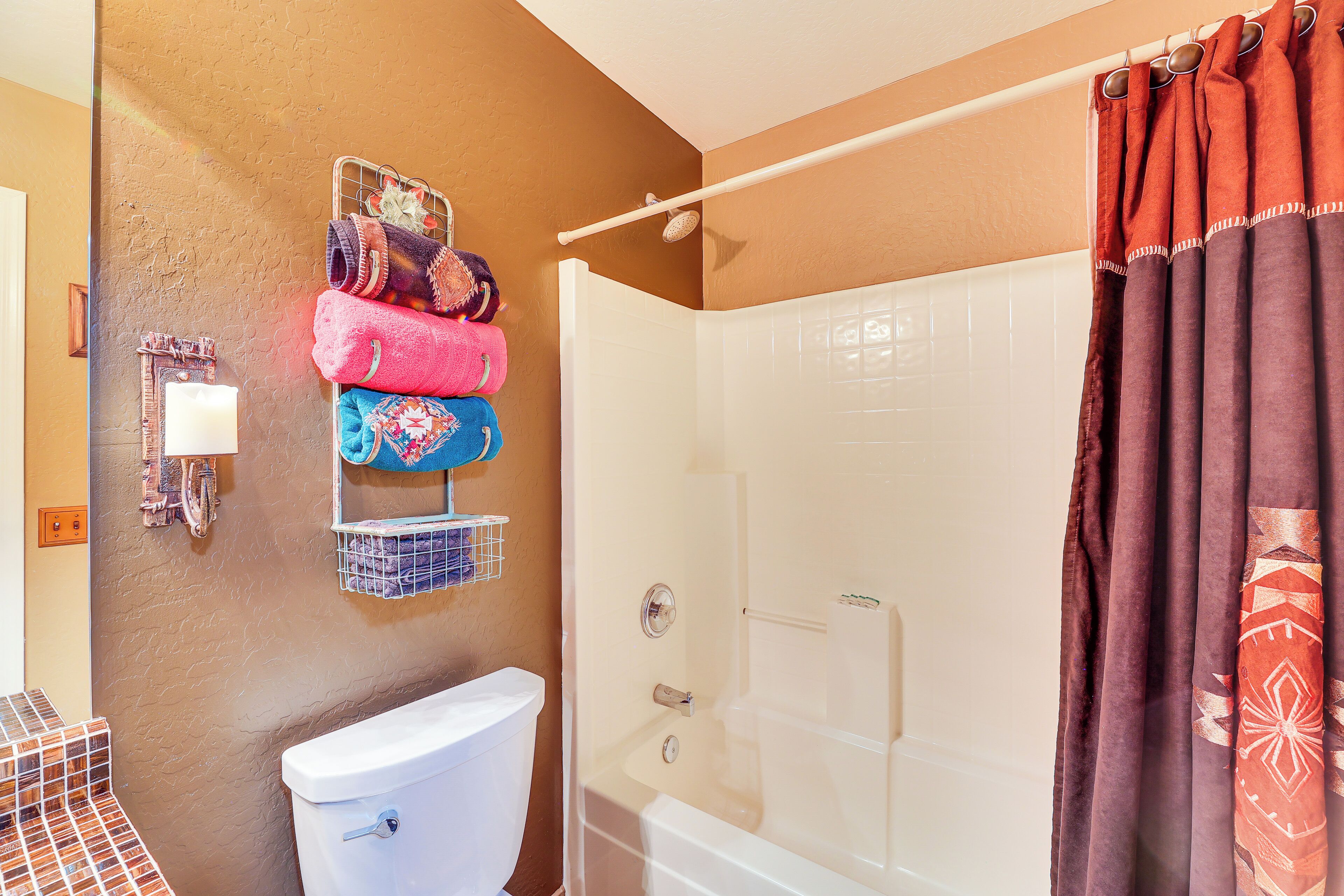 Un baño con inodoro blanco, ducha con puerta de vidrio y toallero con toallas de colores.