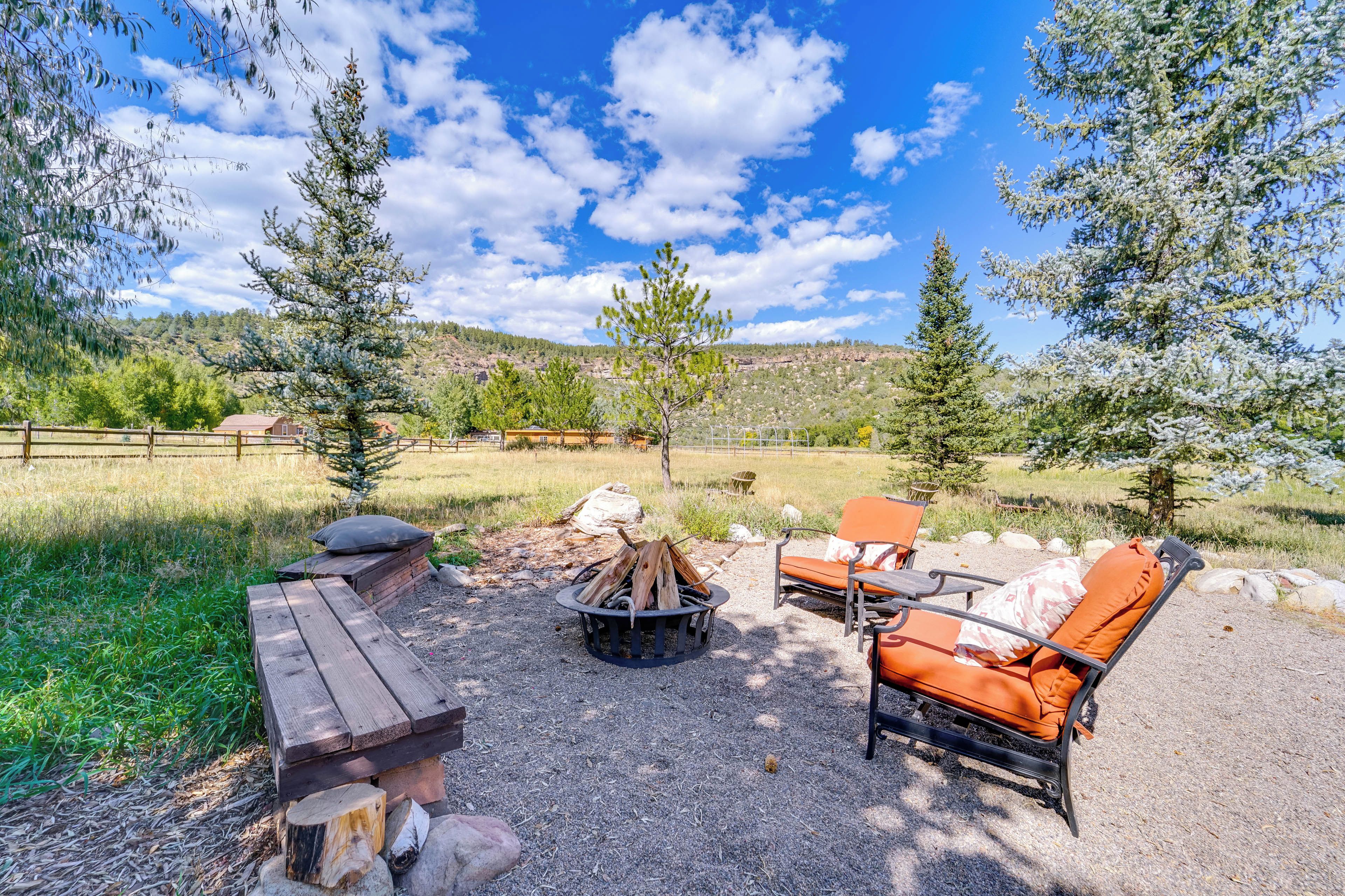 An outdoor seating area with a fire pit, wooden benches, and orange lounge chairs.