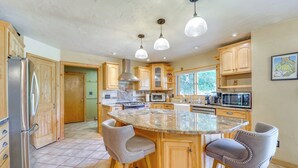 A spacious kitchen with wooden cabinets, a central island with bar stools, stainless steel appliances, and pendant lighting. - Dog-friendly Home w/ Hot Tub & Decks in Durango! (Durango)