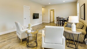 A living room with a ceiling fan, a TV mounted on the wall, a dining area with a table and chairs, and a sofa.