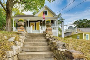 A two-story house with a porch, stone steps, and a flag. - Walk Downtown: Historic Home in Excelsior Springs (Excelsior Springs)