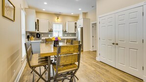 A modern kitchen with white cabinets, a wooden dining table, and a refrigerator.