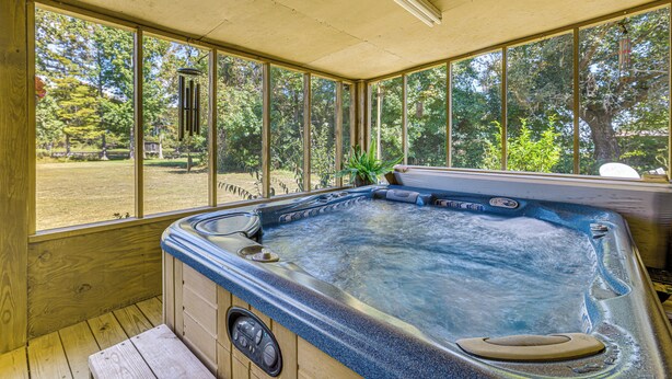 Een hottub met een houten terras en grote ramen met uitzicht op een bebost gebied.