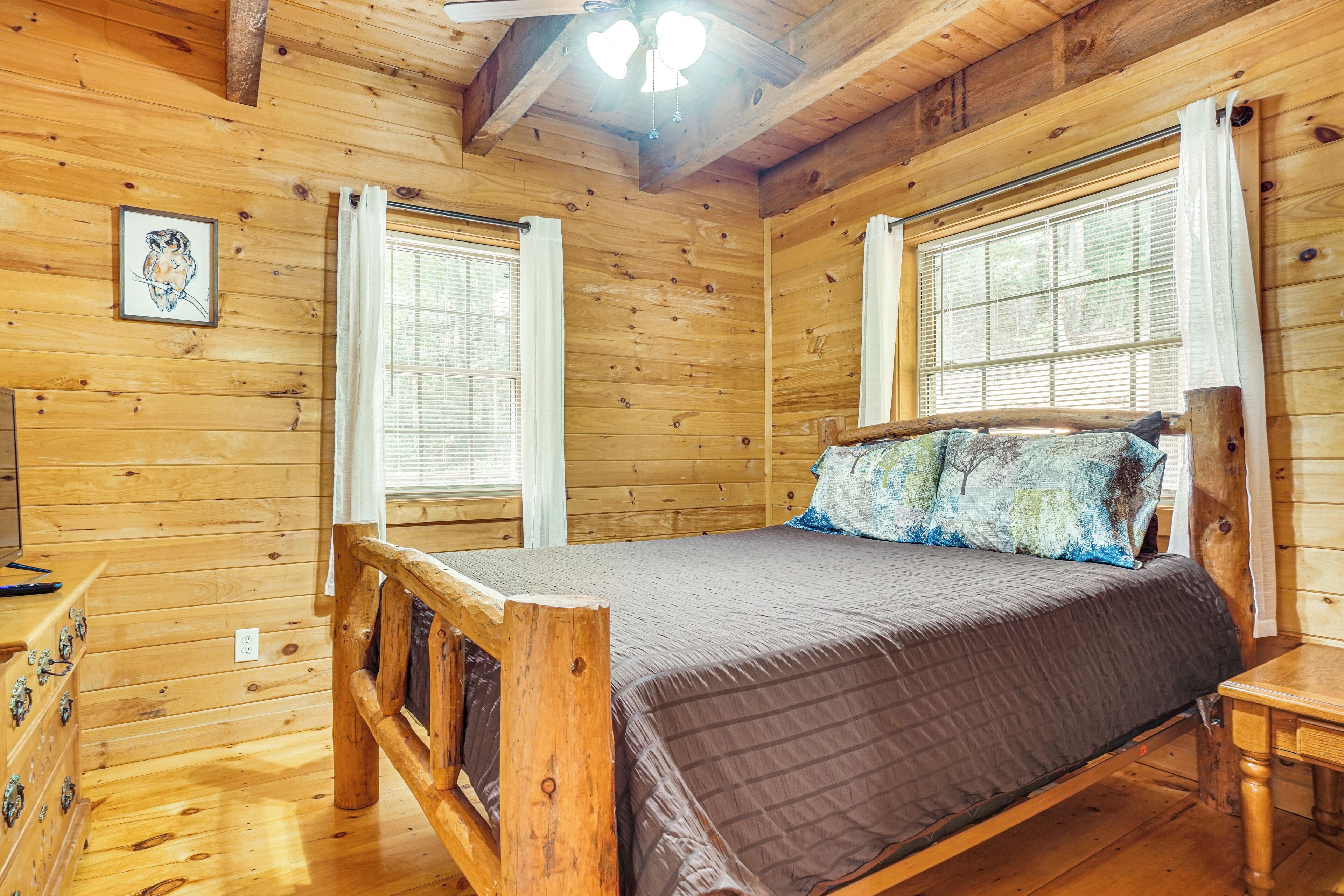 Een slaapkamer in een houten chalet, met een bed, een dressoir en een raam met gordijnen.