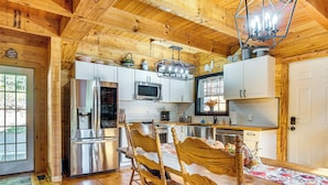 A wooden cabin kitchen with a dining table, chairs, and a chandelier.