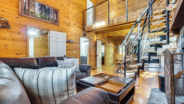 A spacious living room with a large leather sofa, a wooden staircase, and a kitchen area.