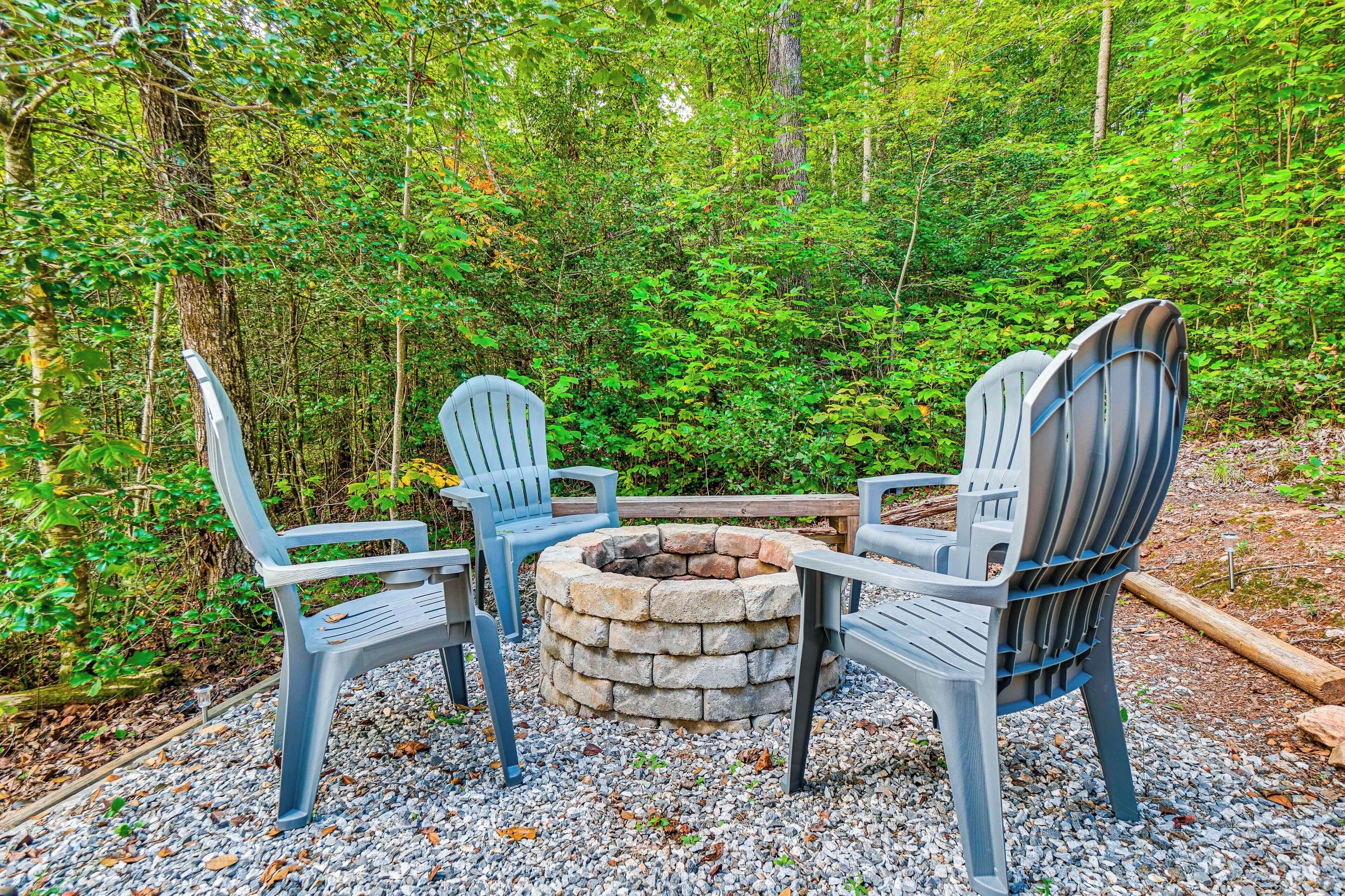 A stone fire pit surrounded by Adirondack chairs in a forested area.